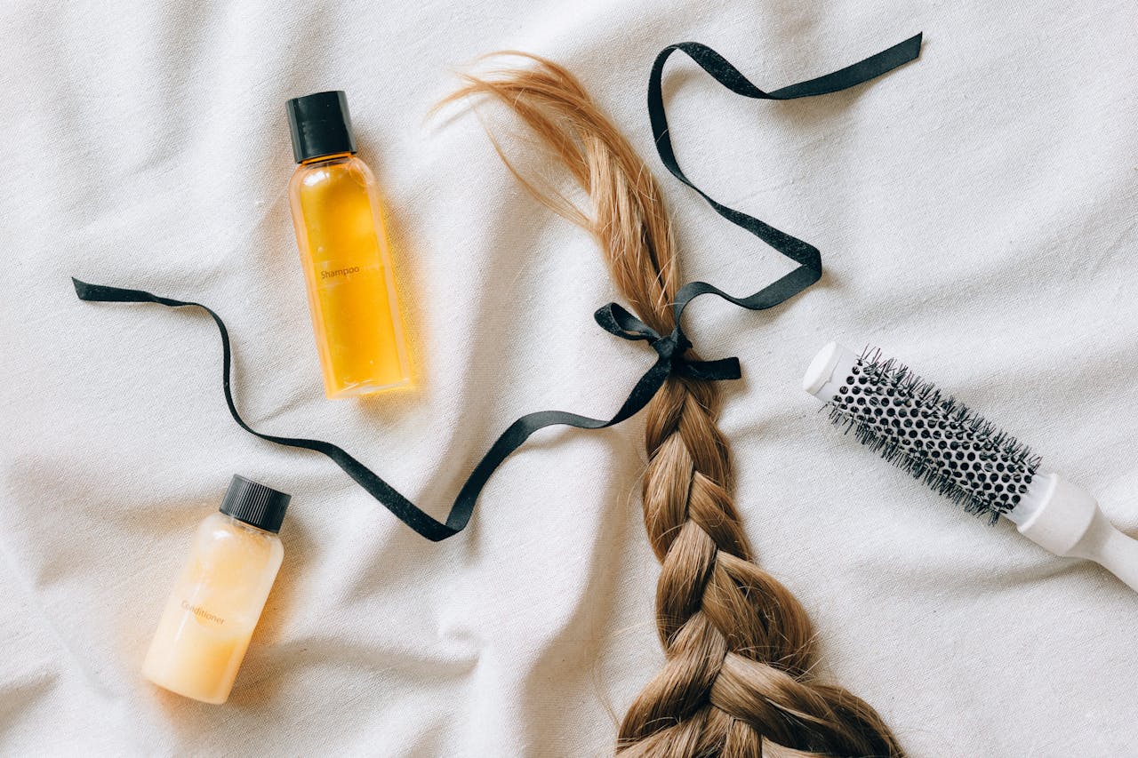hero-gallery-03 Flat lay of braided hair with shampoo bottles and brush on white fabric, conveying beauty and haircare themes.
