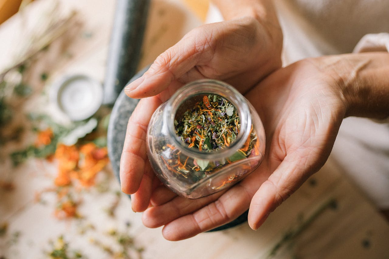 cta-02 Close-up of hands holding a glass jar filled with colorful dried herbs.
